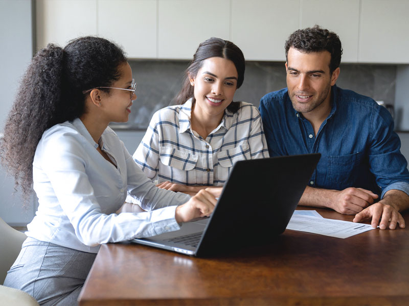 Three people discussing in an office setting while looking at a laptop.