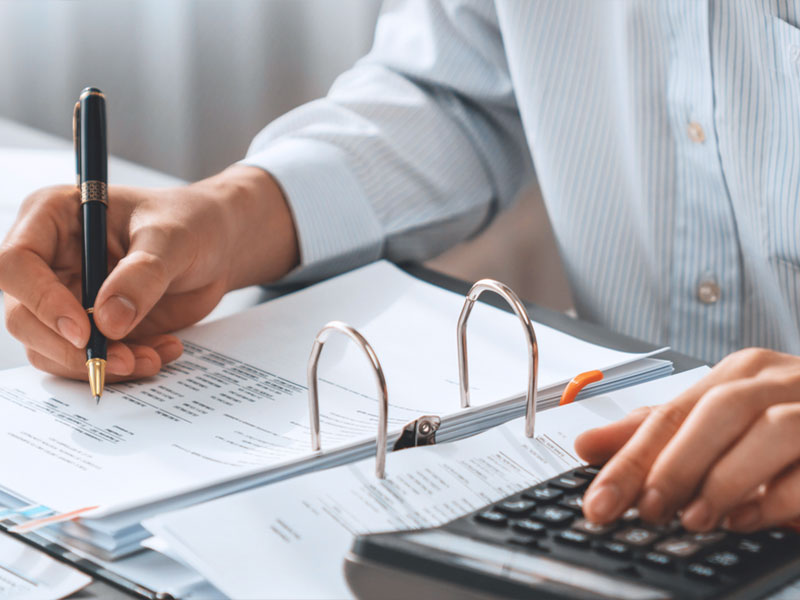 Person analyzing financial documents with pen and calculator.