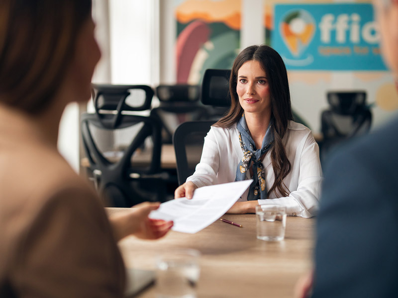 A woman in an office setting receives a document during a business meeting.