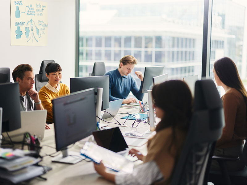 Team collaborating in a modern office with computers and large windows.