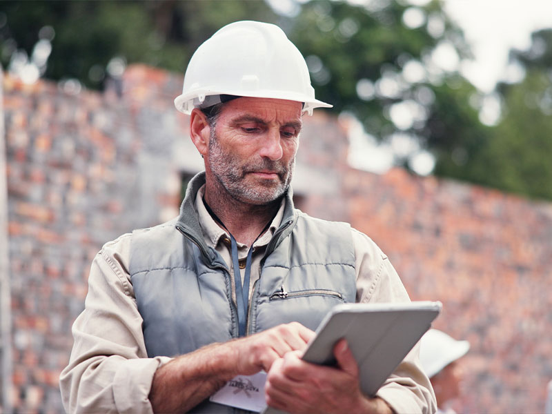 A construction worker in a hard hat using a tablet at a building site.