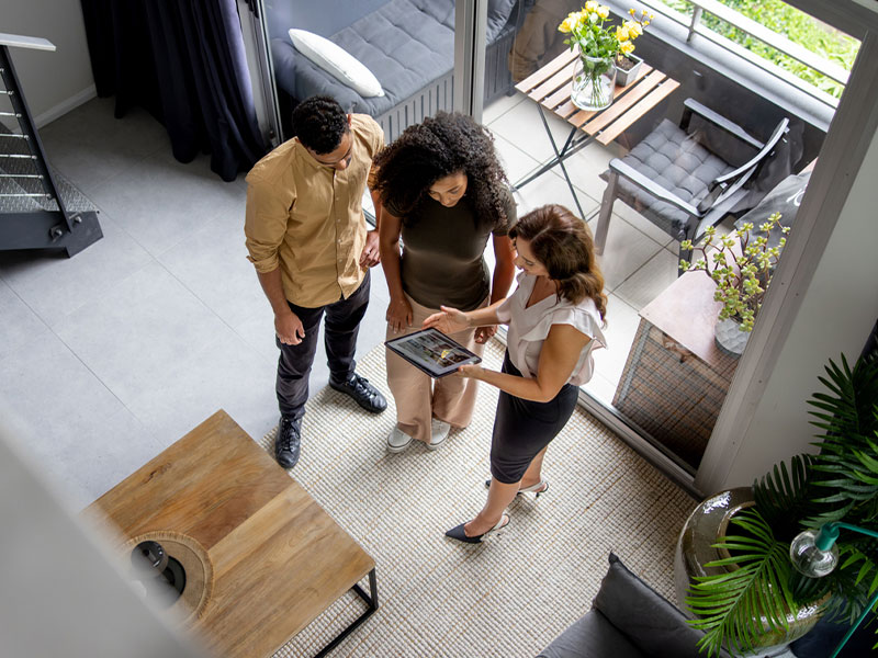 Real estate agent shows couple a property listing on a tablet in a modern living room.