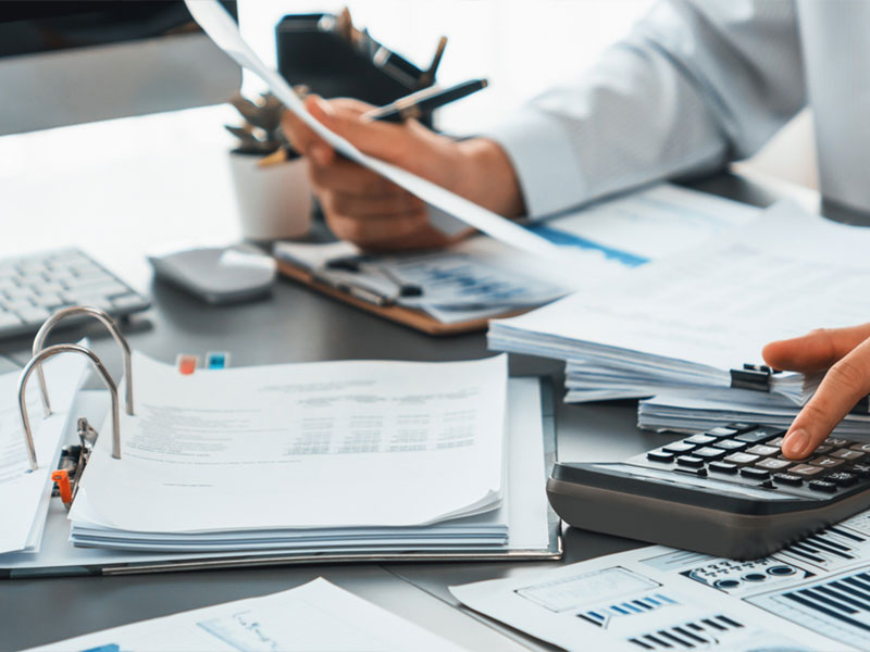 Person using a calculator with financial documents and charts on a desk.