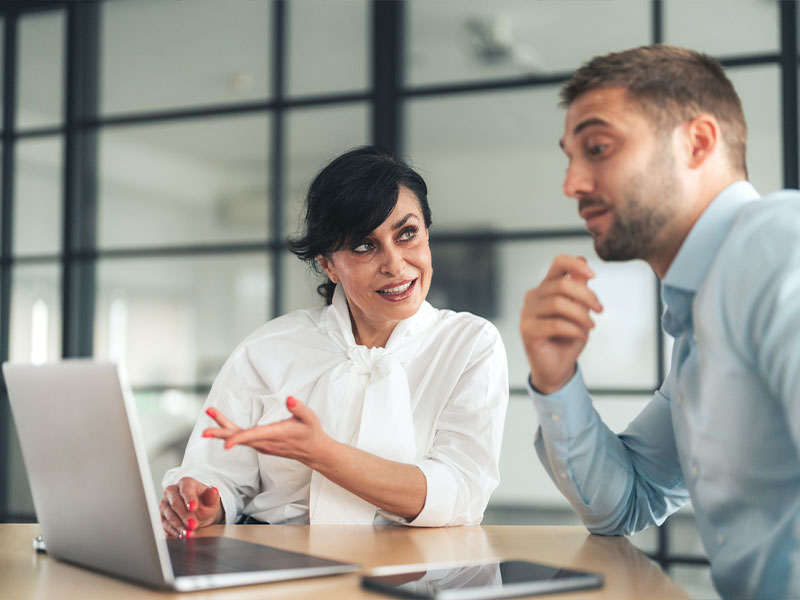A woman and a man having a discussion in an office setting with a laptop.