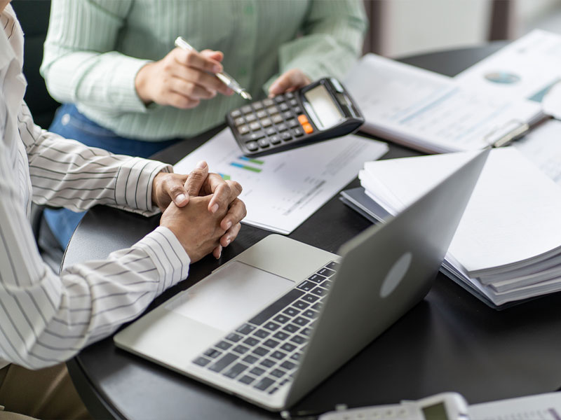 Professionals working at a desk with laptop, calculator, and documents.