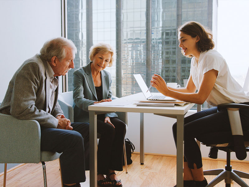 A woman consulting with an older couple in an office setting, discussing documents.