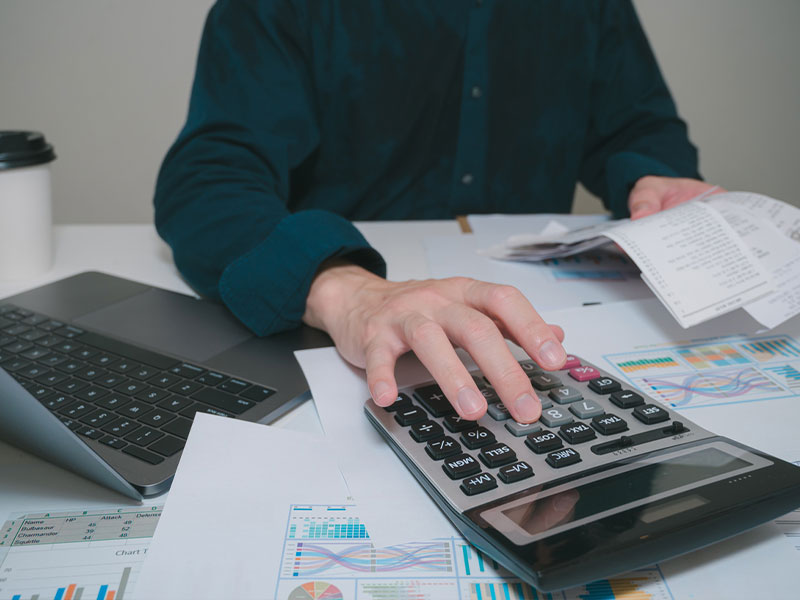 Person using a calculator at a desk with charts and receipts.