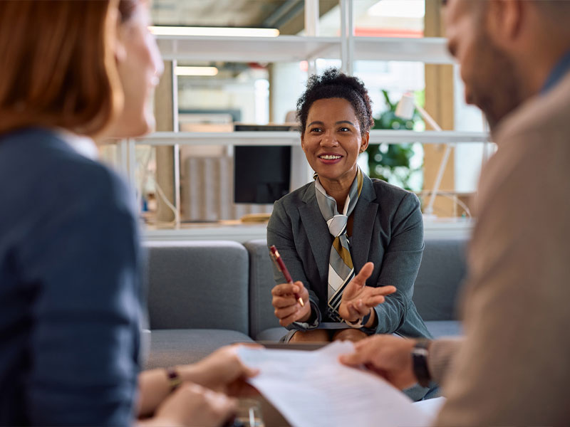 Business meeting with smiling woman in an office setting, discussing documents with two colleagues.