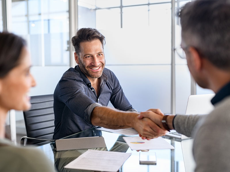 A man smiling and shaking hands at a business meeting in a modern office.