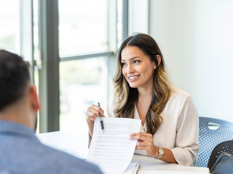 Woman holding a document, engaged in a meeting, seated in a bright office setting.