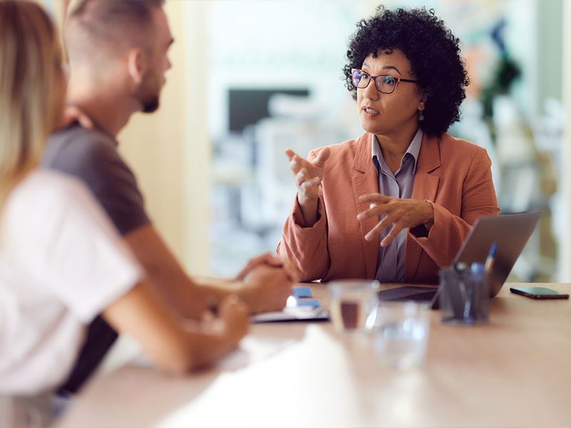 A woman in a business meeting with a laptop, discussing with a man and a woman.