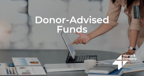 A person pointing at a tablet screen on a table with documents, captioned Donor-Advised Funds.