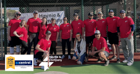 Haynie team in red shirts at a baseball field with a Top Workplaces 2022 award.