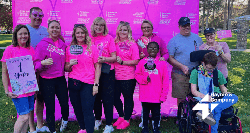Group celebrating cancer awareness event, wearing pink shirts, holding survivor sign and Haynie banner.