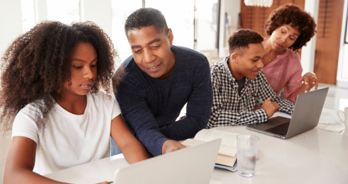 A family of four working together on laptops at home.