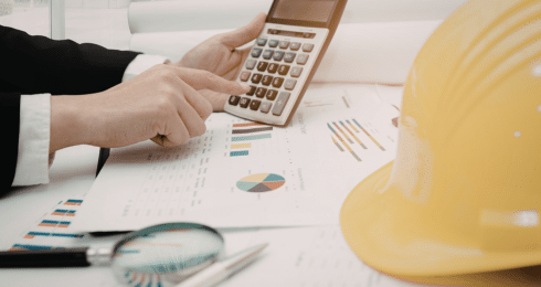 Person using calculator with construction plans and hard hat nearby.