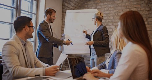Team meeting with people discussing a graph on a flip chart in a bright office room.
