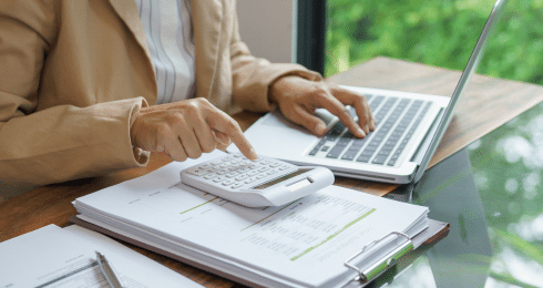 Person using a laptop and calculator while reviewing financial documents at a desk.