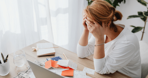 A person stressed over bills and paperwork at a desk with a laptop.