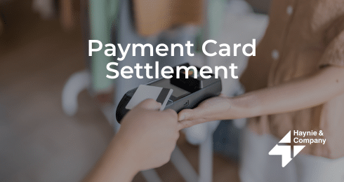Payment card settlement with a POS terminal, hand holding a card. Haynie logo.