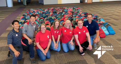 A group of individuals in front of rows of colorful backpacks, Haynie logo visible.