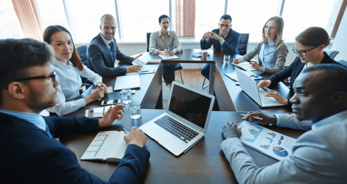 Business team in a meeting around a conference table with laptops and documents.