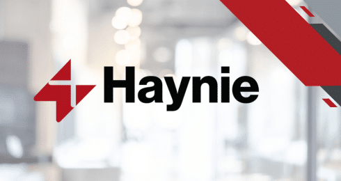 Haynie logo with red geometric design on a blurred office background.