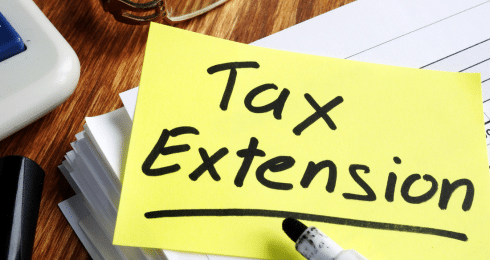 Tax extension note on a desk with pen, calculator, and documents.