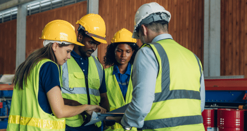 Workers in safety vests and helmets discussing plans in a warehouse.