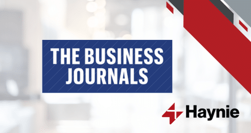 The Business Journals logo with Haynie branding on a light blurred background.