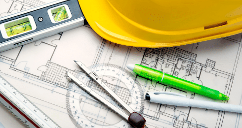 Architectural plans with compass, ruler, pen, and yellow hard hat.