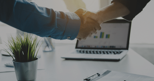 Handshake between two people in an office setting near a laptop.