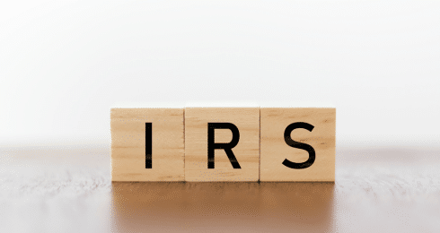 Wooden blocks spelling IRS on a flat surface, blurred white background.