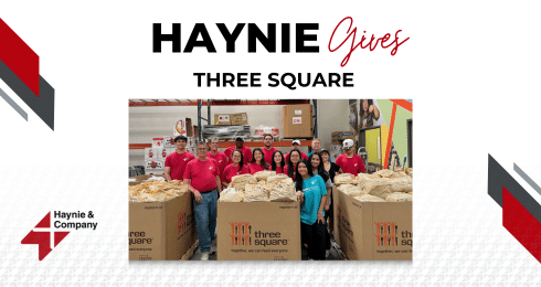 Group of people in red shirts volunteering at Three Square food bank, surrounded by large boxes of packaged food.