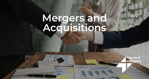Handshake over business documents signifying mergers and acquisitions, Haynie logo visible.