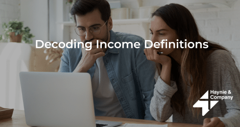 Decoding income definitions on laptop with Haynie logo in office.