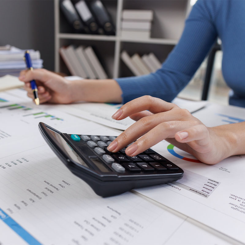 A person calculating finances with a calculator, analyzing charts and graphs at a desk.