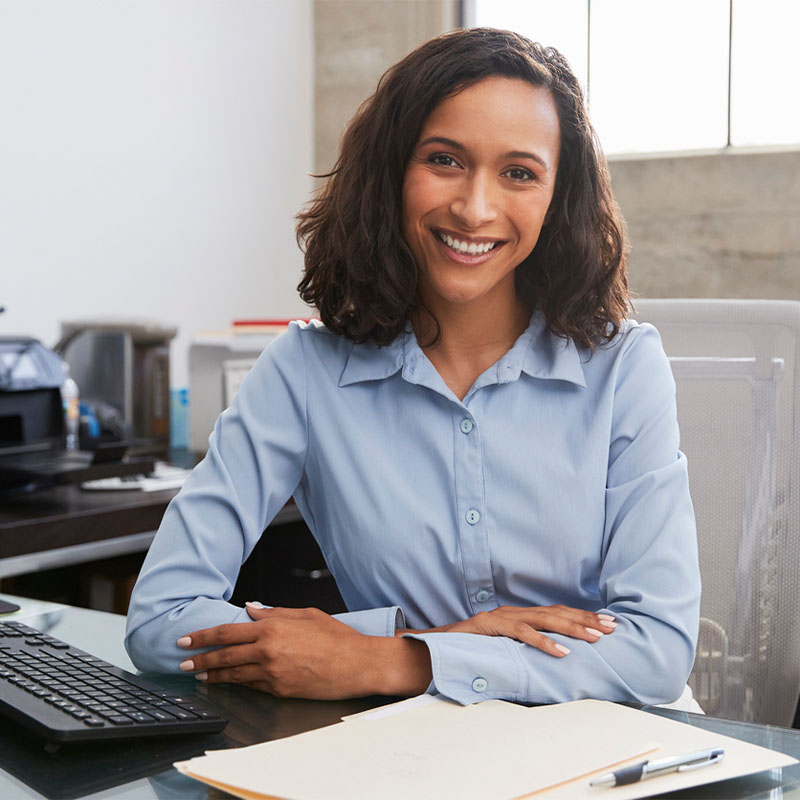 Person in a blue shirt smiling at a desk with a keyboard and papers.