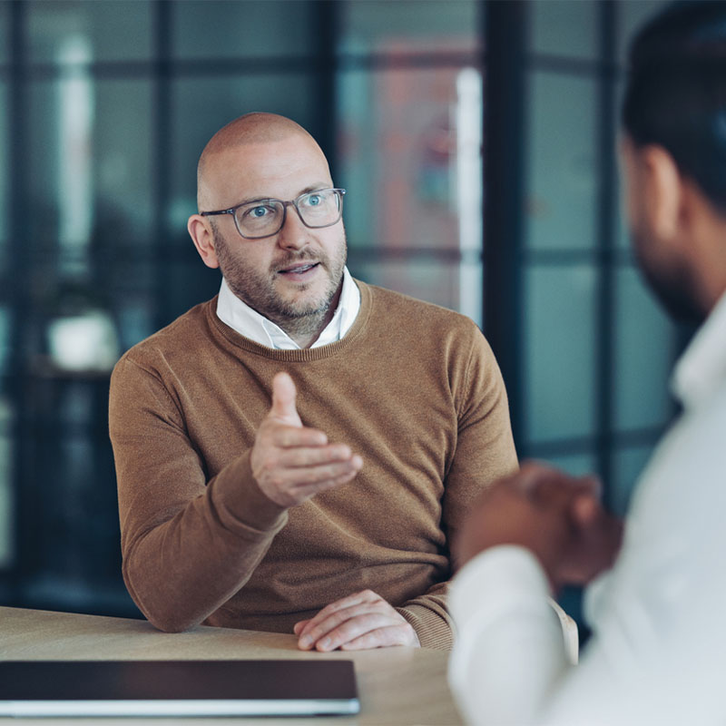 Bald man in glasses discussing with a colleague in an office setting.