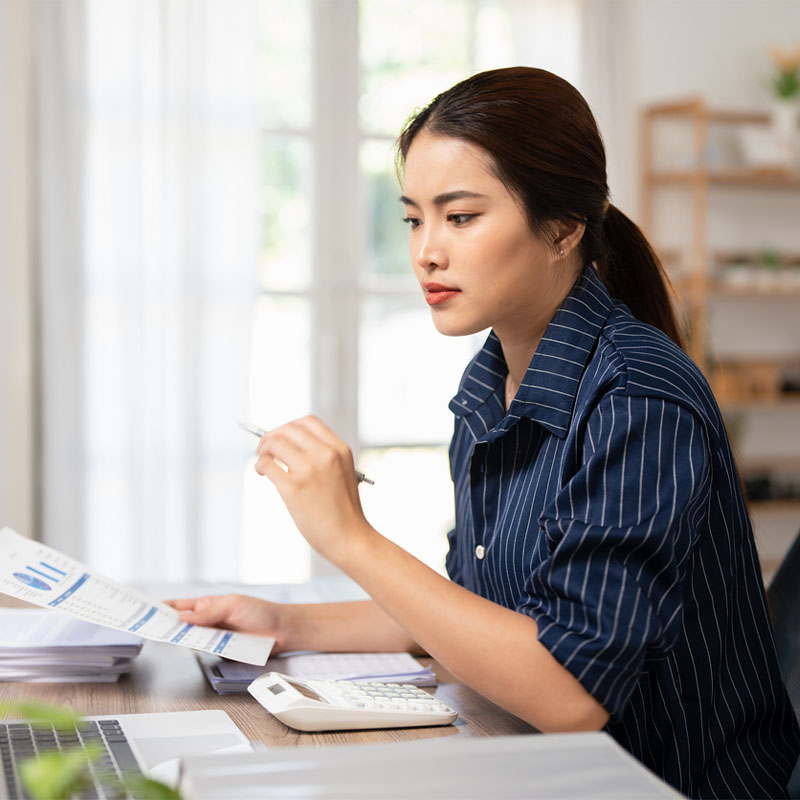 Woman in striped shirt working with documents at a desk, using a calculator.
