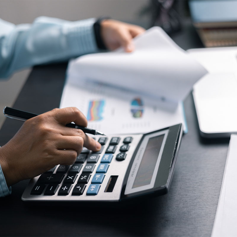 Person working with calculator and financial documents at desk.