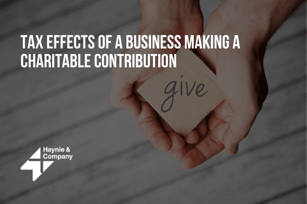 Hands holding a card with 'give' text, relating to business charitable contributions and tax effects.