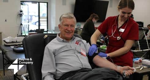 Man donating blood at a Haynie event, assisted by a nurse in red scrubs.