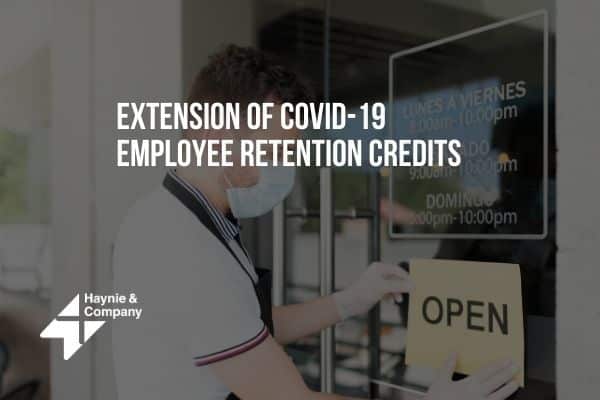 Person wearing mask placing Open sign on storefront, text on COVID-19 employee retention credits.