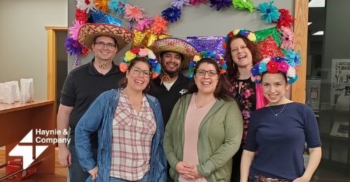 Group of six people wearing colorful floral hats and smiling at Haynie office.