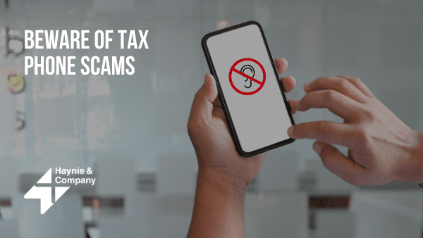 Hands holding a smartphone displaying a warning about tax phone scams, with Haynie logo.