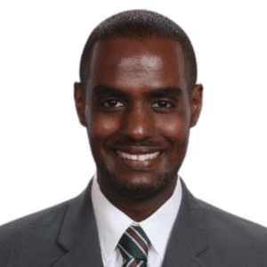A man wearing a suit and tie, smiling against a white background.