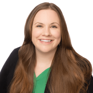 A smiling woman with long hair and a green top under a black blazer.