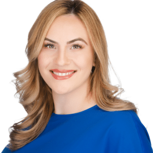 A woman with blonde hair in a blue top, smiling against a white background.