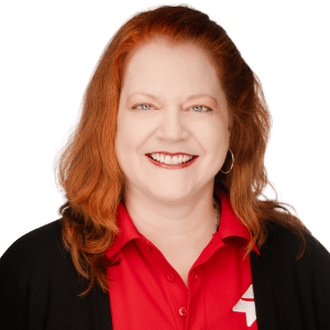 A woman with red hair smiling, wearing a red shirt and black cardigan, on a white background.